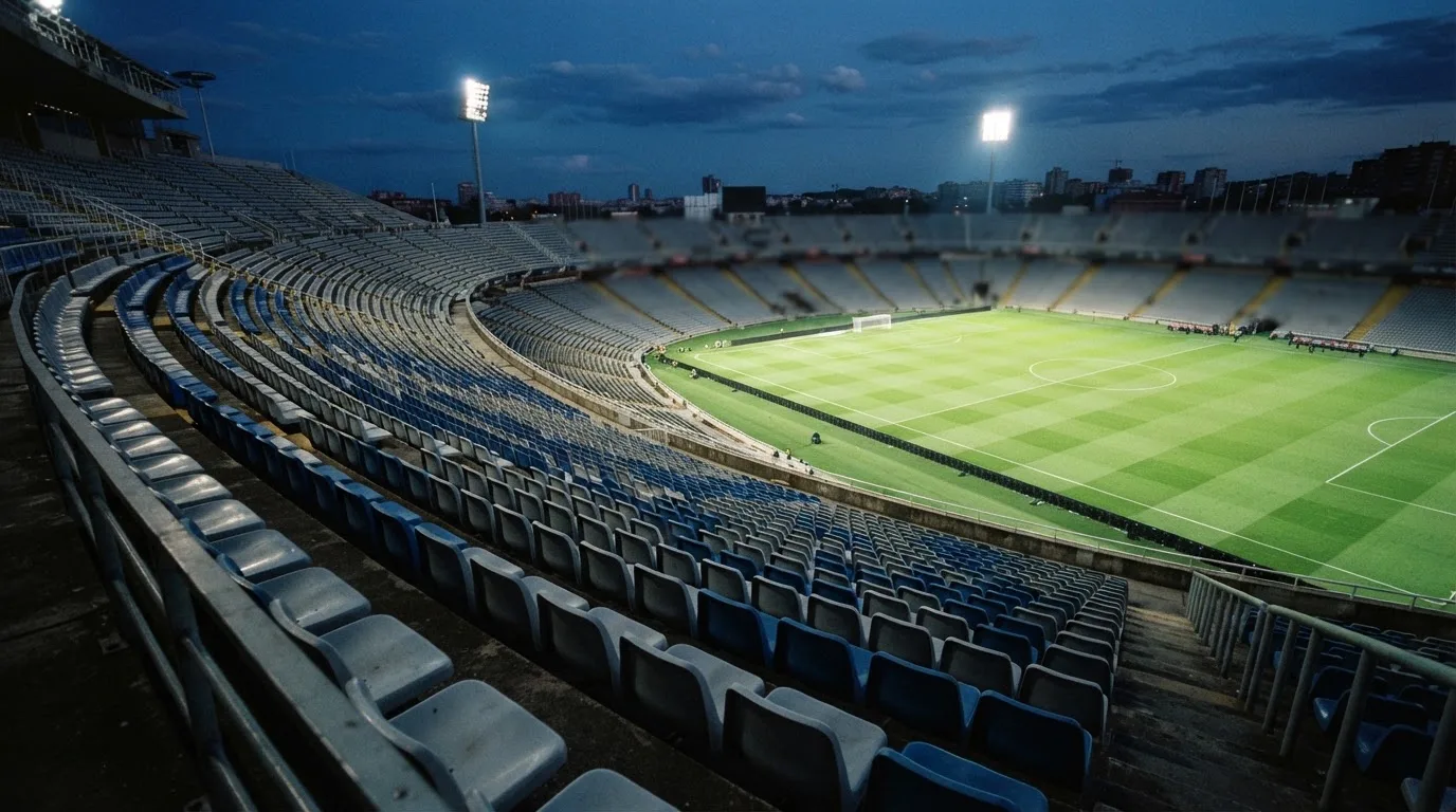 Rzędy pustych plastikowych krzesełek na trybunie stadionu widziane z górnego rzędu, opadają łukiem ku zielonej murawie pod reflektorami.