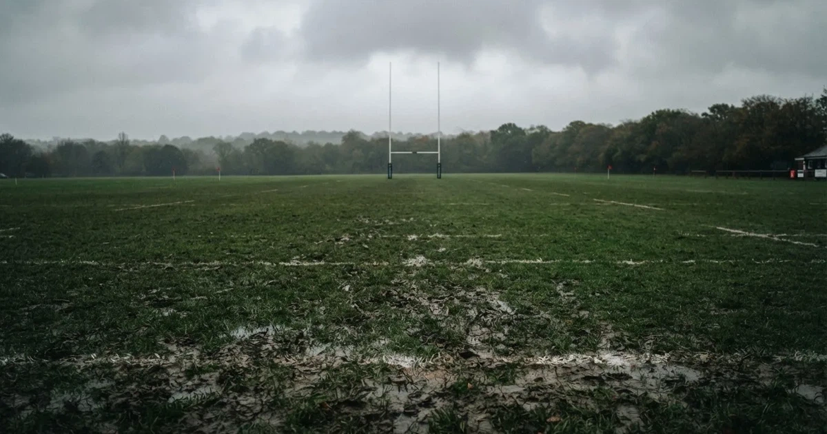 Boisko do rugby ze słupami bramki w oddali pod pochmurnym niebem, mokra trawa i ślady butów.