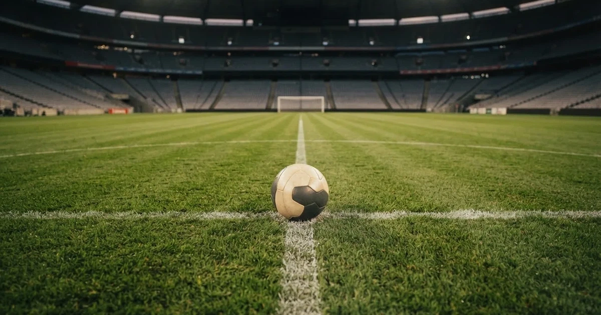 Piłka nożna leżąca na środku murawy w pustym stadionie przed meczem, rzędy siedzisk w półmroku.